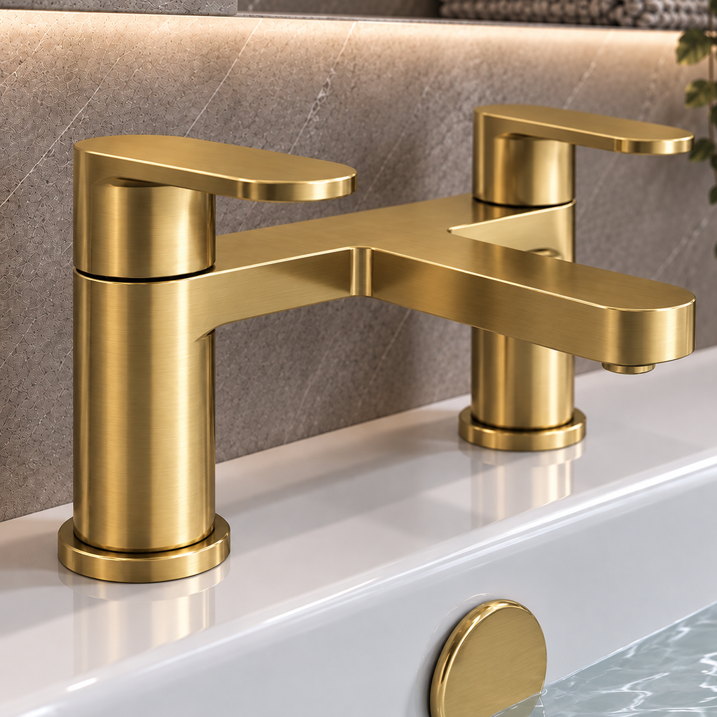 A modern two-handle bathroom faucet in brushed gold metal, mounted on a white sink with a textured gray stone backsplash behind it.