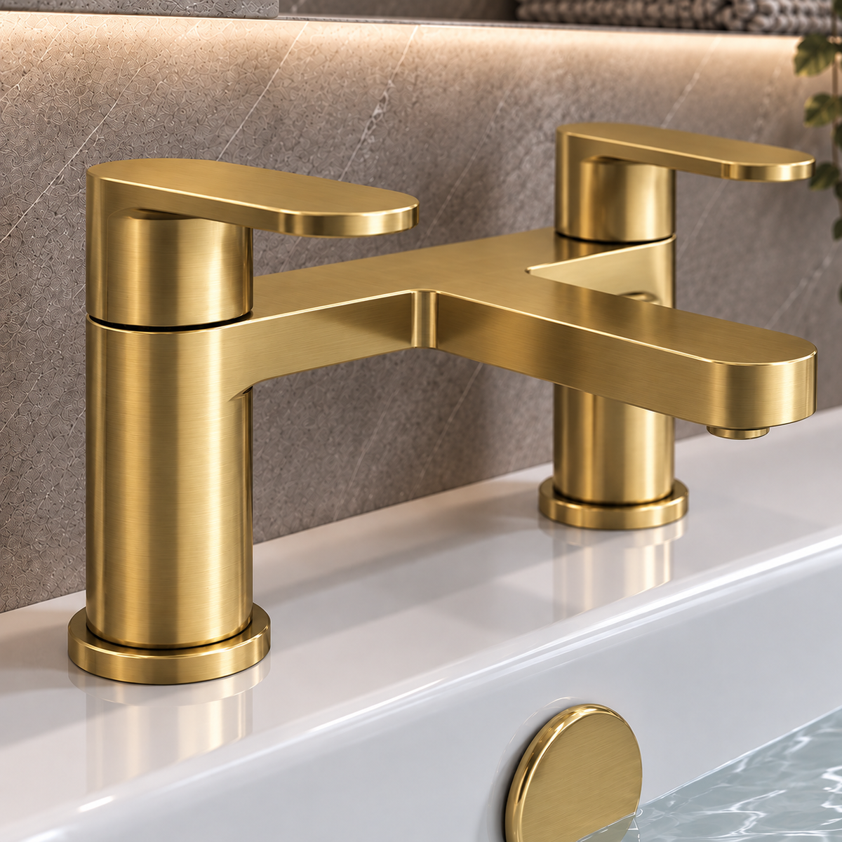 A modern two-handle bathroom faucet in brushed gold metal, mounted on a white sink with a textured gray stone backsplash behind it.