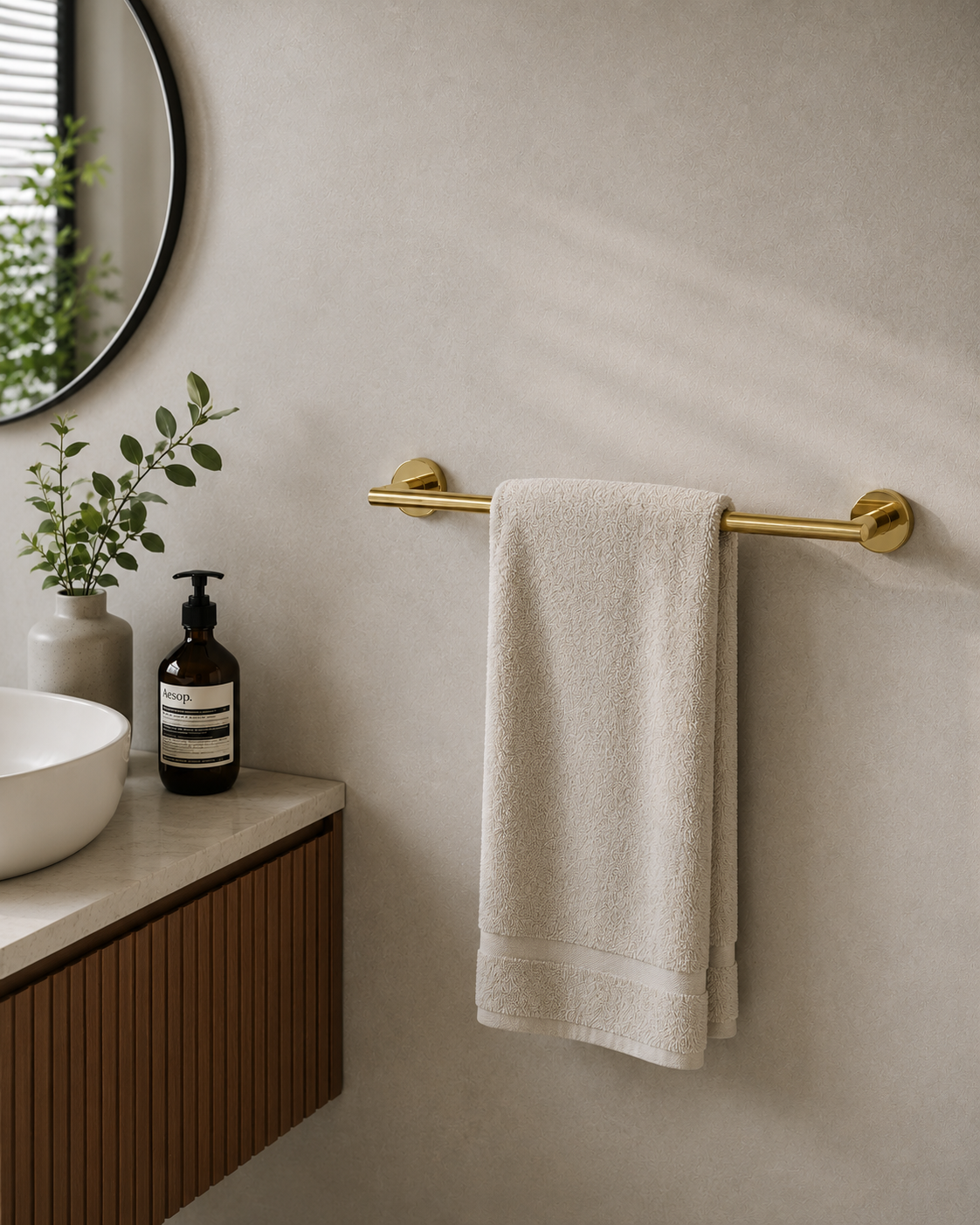Bathroom setting with a towel hanging on a gold towel rack, a plant, and a bottle.