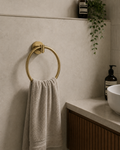 Gold towel ring with a beige towel on a bathroom wall, next to a sink and bottles.