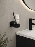 Bathroom setting with a black toothbrush holder on a gray wall, holding a toothbrush and tube of toothpaste.