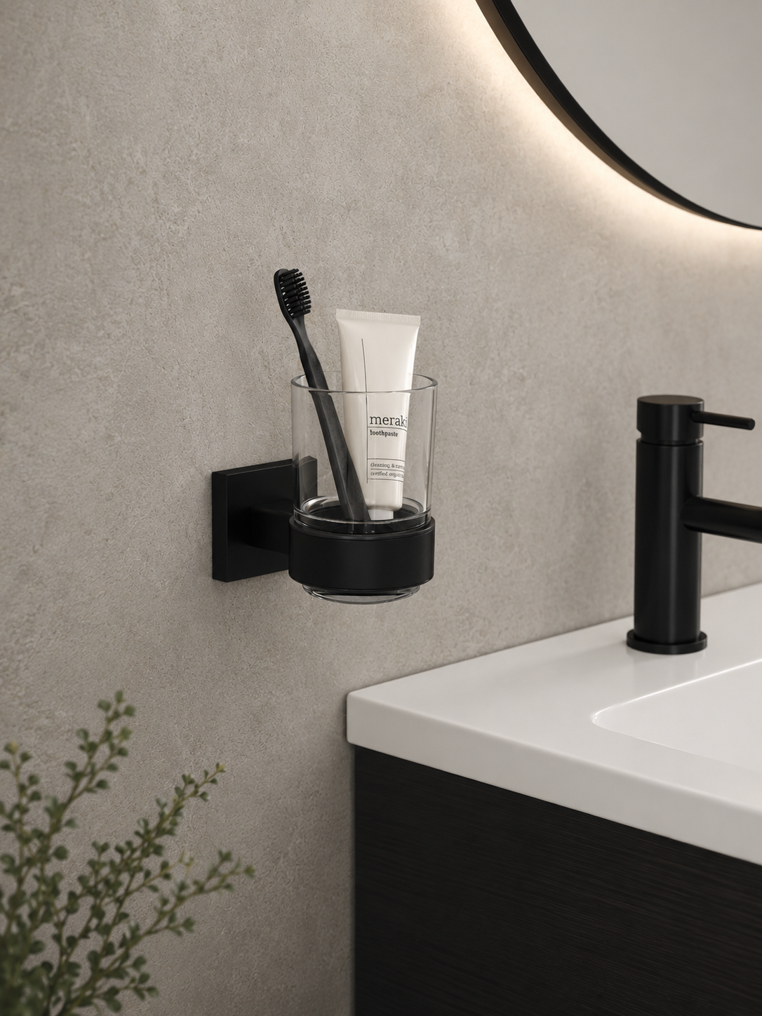 Bathroom setting with a black toothbrush holder on a gray wall, holding a toothbrush and tube of toothpaste.