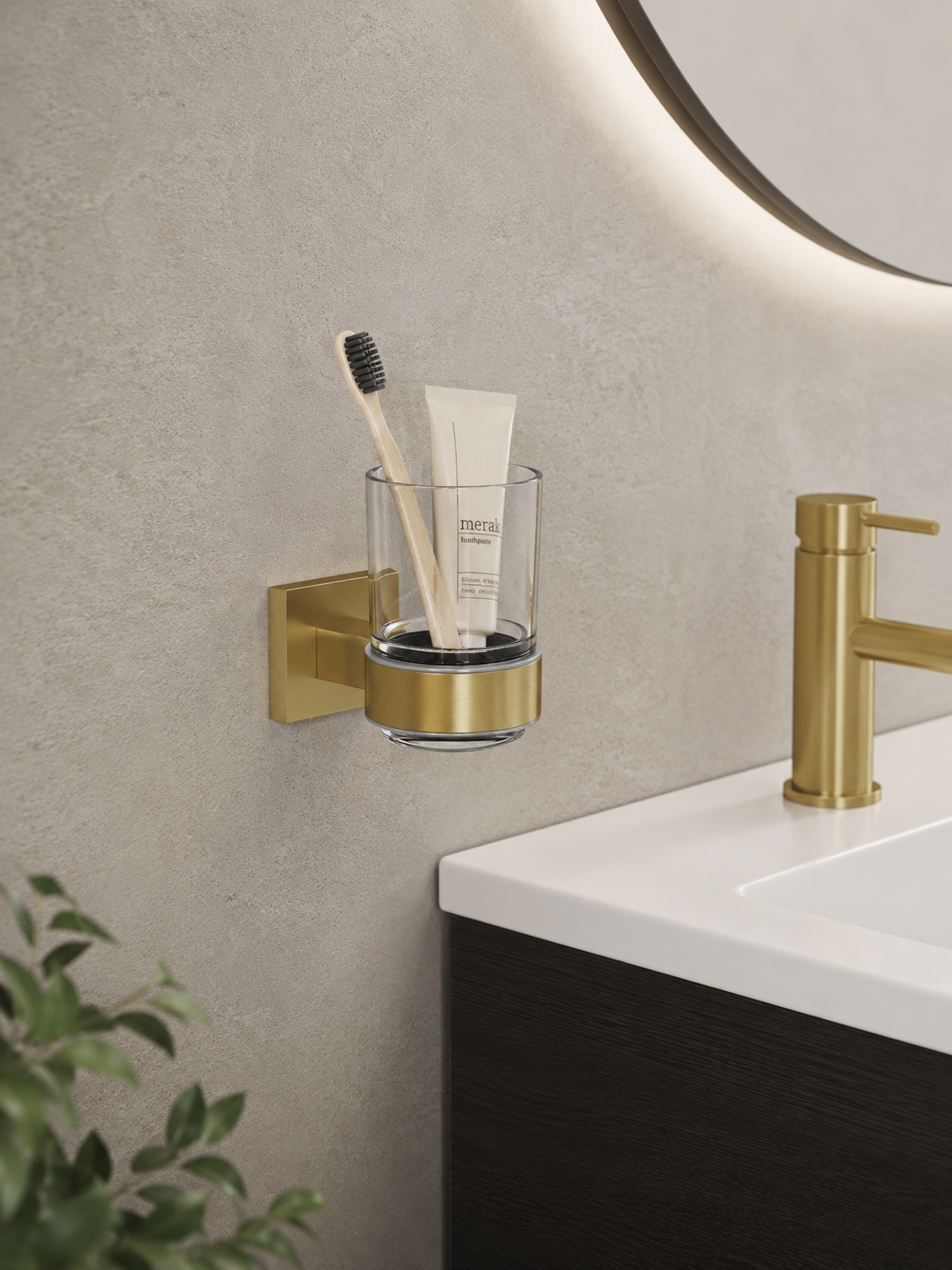 Bathroom setting with a gold wall-mounted cup holder holding a toothbrush and tube of toothpaste, next to a sink.