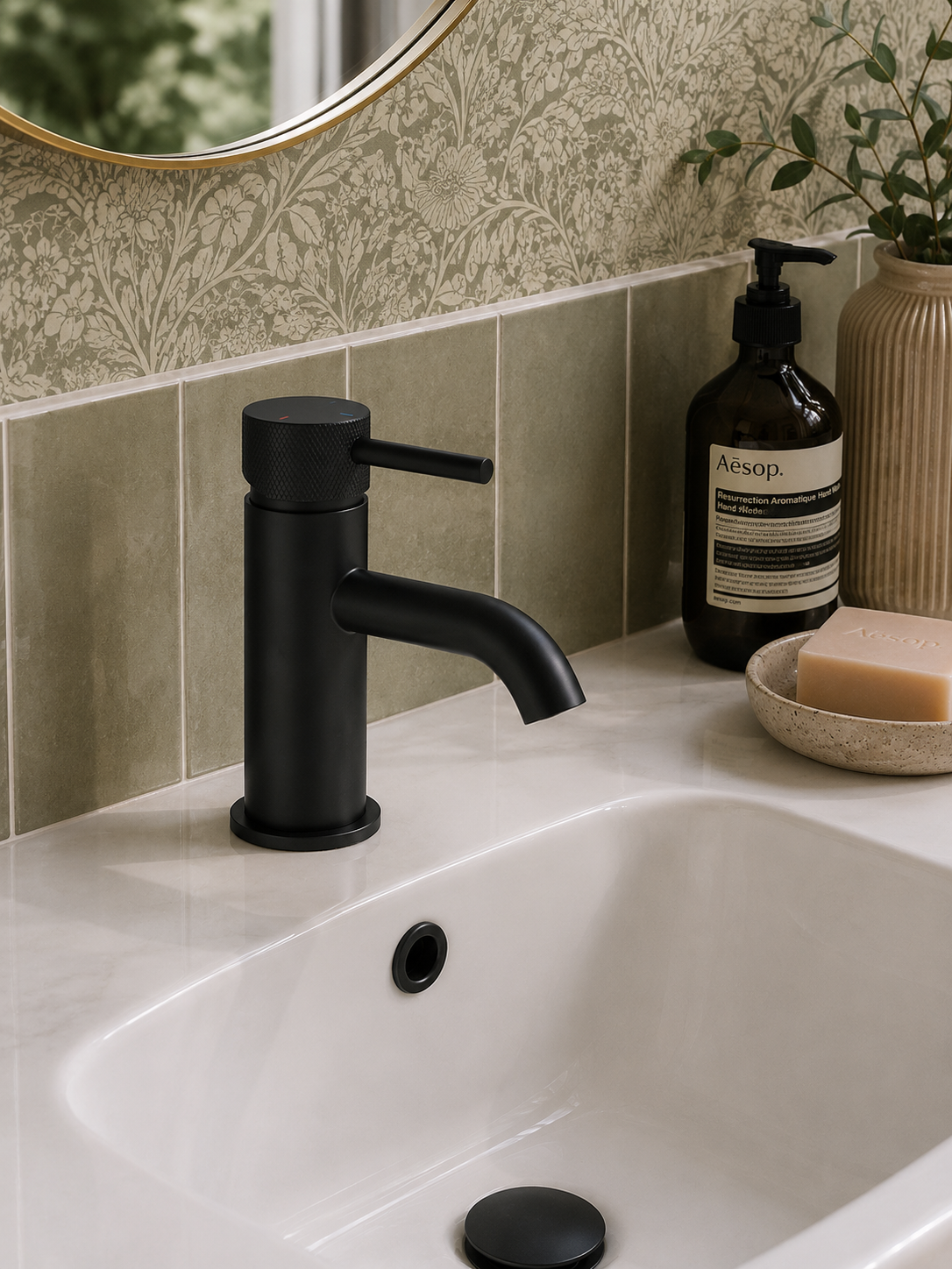 Black faucet on a bathroom sink with Aesop products in the background