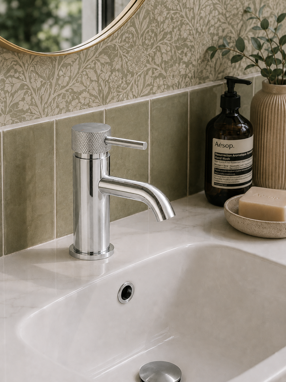Bathroom sink with chrome faucet, Aesop bottle, and soap on a tiled wall background