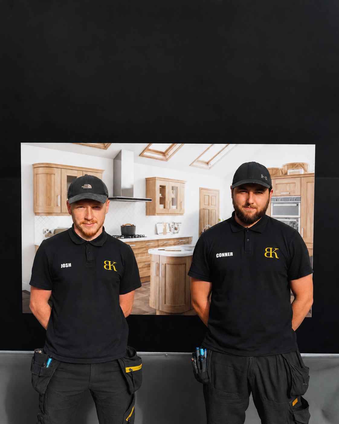 Two men in black uniforms with a logo standing in front of a kitchen display.